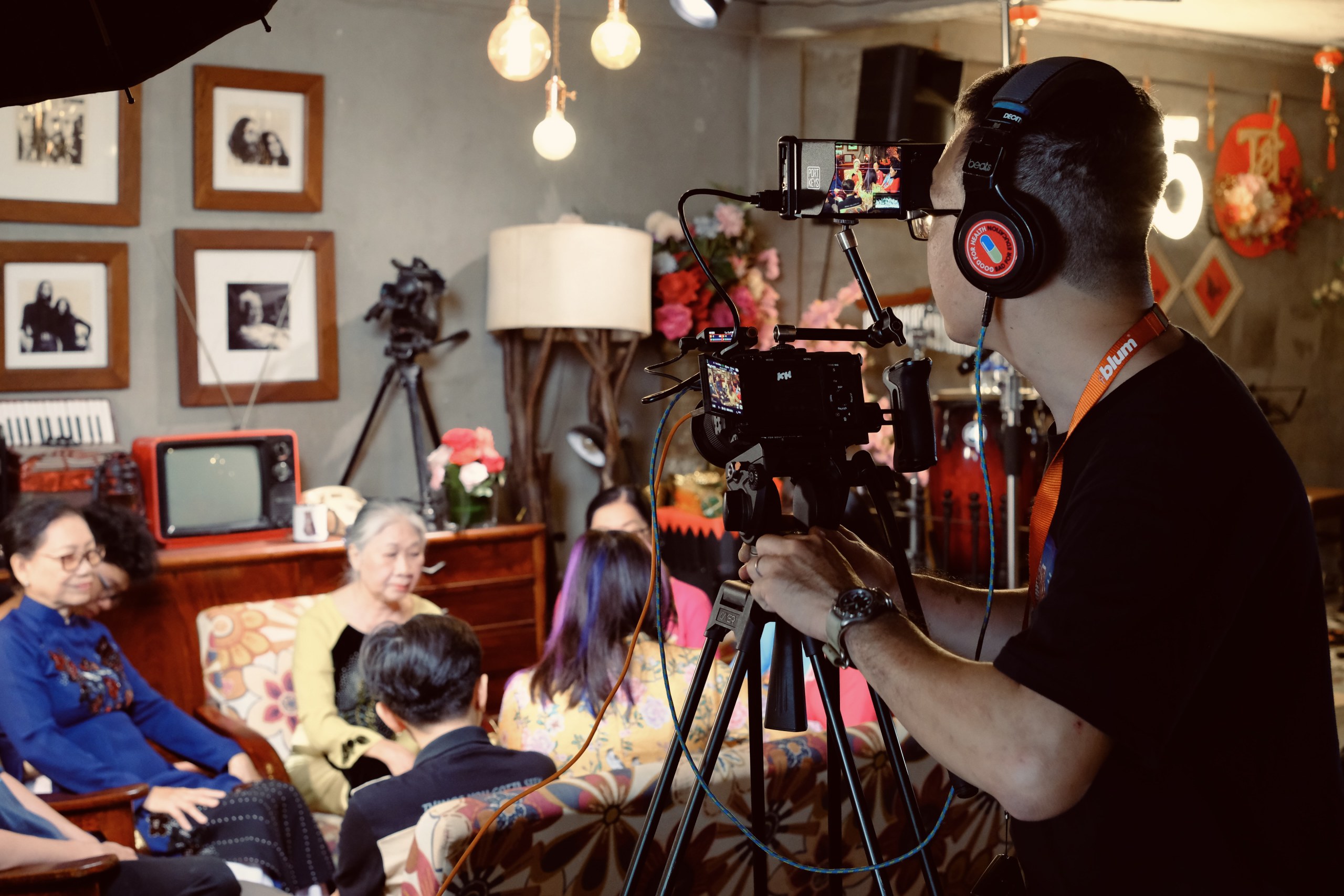 A camera operator wearing headphones films three generations of a family seated together in their living room